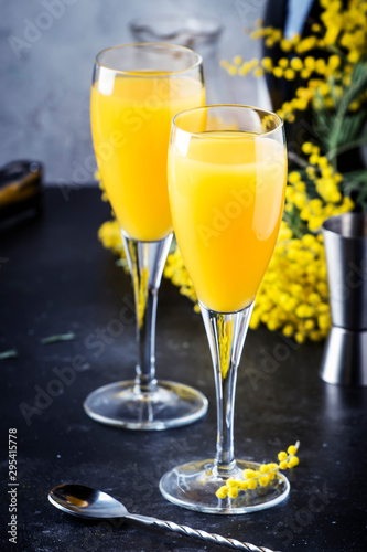 Mimosa alcohol cocktail with orange juice and cold dry champagne or sparkling wine in glasses, gray bar counter background with yelow flowers, copy space, selective focus