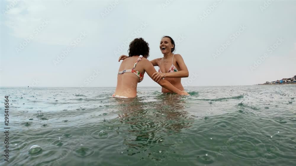 Slow motion of teo female friends having fun, dancing and laughing in the sea while raining Slow motion of teo female friends having fun, dancing and laughing in the sea while raining