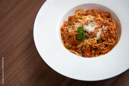 Spaghetti in tomato sauce, served on a plate, parsley in a white dish, on a brown wooden floor, Italian food