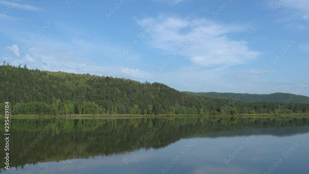 Summer sunny day by river. Blue sky, calm river and mountains covered by forest. Natural landscape. Environmental Safety. 4K video Summer sunny day by river. Blue sky, calm river and mountains covered by forest. Natural landscape. Environmental Safety. 4K video