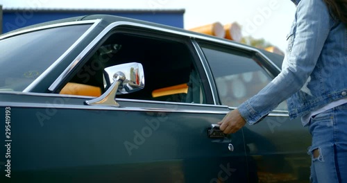 brunette woman is opening door and sitting inside old car in sunny windy day