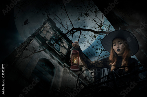 Halloween witch holding ancient lamp standing over grunge castle, dead tree, bird fly, full moon and cloudy spooky sky, Halloween mystery concept