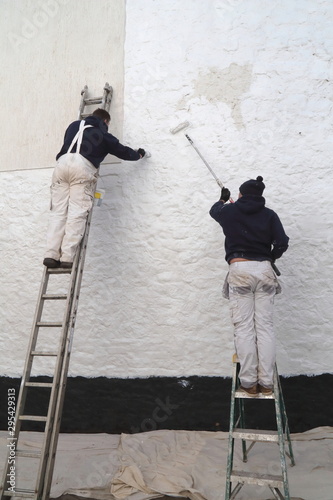Workers painting facade while standing on the ladder