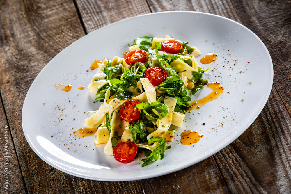 Pasta with tomatoes and arugula on wooden table Pasta with tomatoes and arugula on wooden table