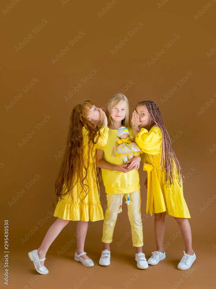 children of girlfriend with long hair in yellow fashionable clothes share a secret on a brown background children of girlfriend with long hair in yellow fashionable clothes share a secret on a brown background