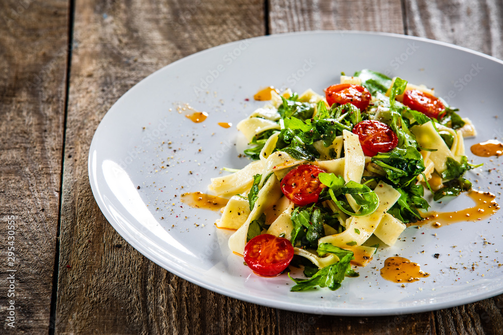 Pasta with tomatoes and arugula on wooden table Pasta with tomatoes and arugula on wooden table