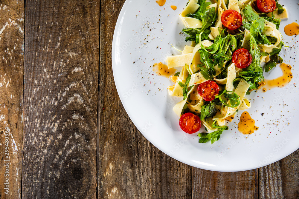 Pasta with tomatoes and arugula on wooden table Pasta with tomatoes and arugula on wooden table