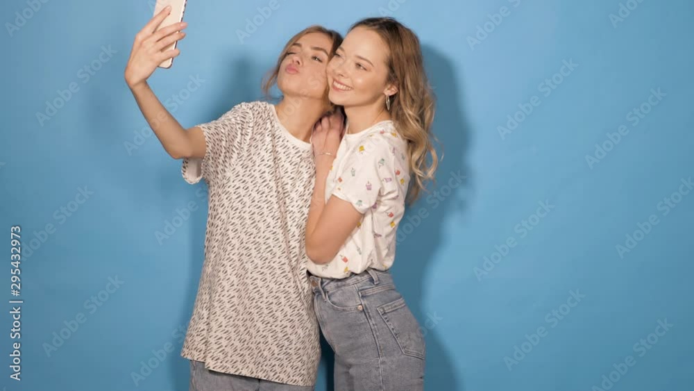Two beautiful smiling girls.Women in summer hipster clothes taking selfie self portrait photos on smartphone. Models making funny faces and having fun in studio.They show tongue and make duck face Two beautiful smiling girls.Women in summer hipster clothes taking selfie self portrait photos on smartphone. Models making funny faces and having fun in studio.They show tongue and make duck face