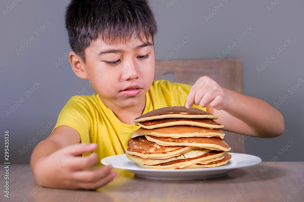 Young boy having pancakes breakfast. 8 years old happy excited child sitting on table eating huge pile of pancakes smiling in sugar abuse and unhealthy nutrition Young boy having pancakes breakfast. 8 years old happy excited child sitting on table eating huge pile of pancakes smiling in sugar abuse and unhealthy nutrition