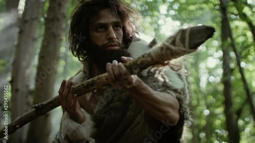Portrait of Primeval Caveman Wearing Animal Skin and Fur Hunting with a Stone Tipped Spear in the Prehistoric Forest. Prehistoric Neanderthal Hunter Ready to Throw Spear in the Jungle photo