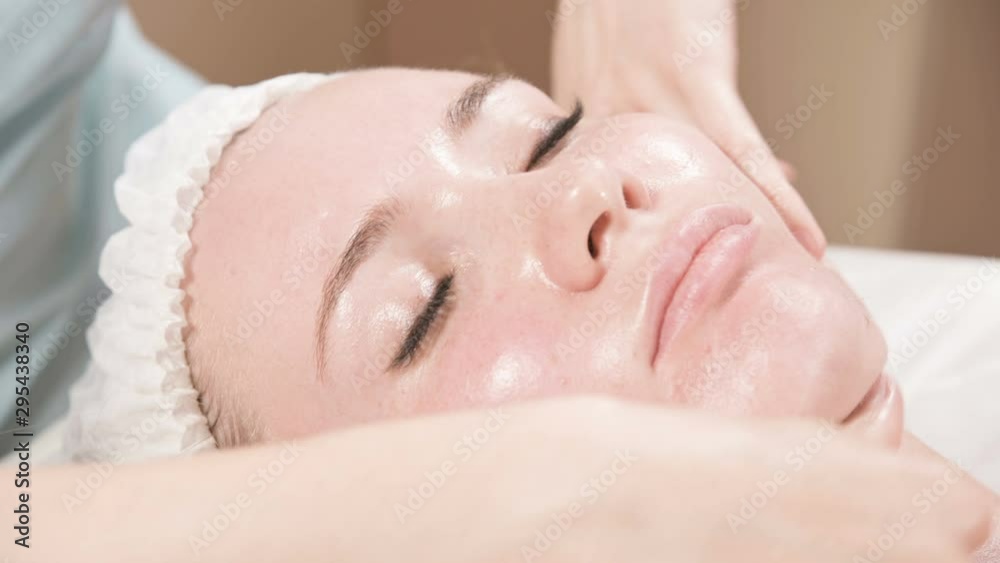 Close-up Spa facial Massage. Girl professional massage therapist does a relaxing facial massage to an attractive client of a spa salon Close-up Spa facial Massage. Girl professional massage therapist does a relaxing facial massage to an attractive client of a spa salon