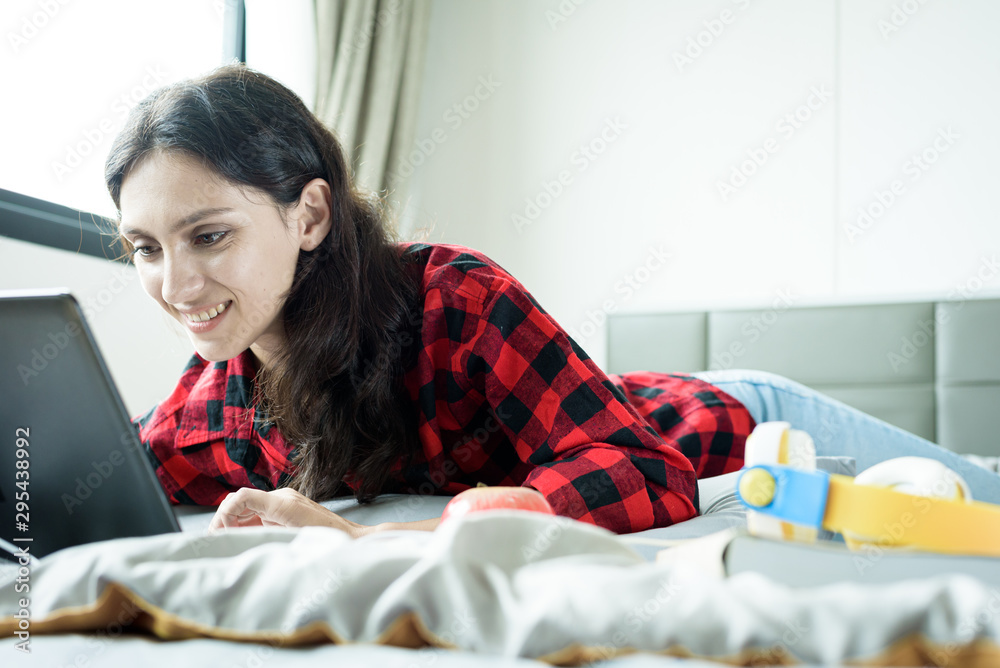 Beautiful woman working on a laptop and lying down on the bed at a condominium in the morning. Beautiful woman working on a laptop and lying down on the bed at a condominium in the morning.