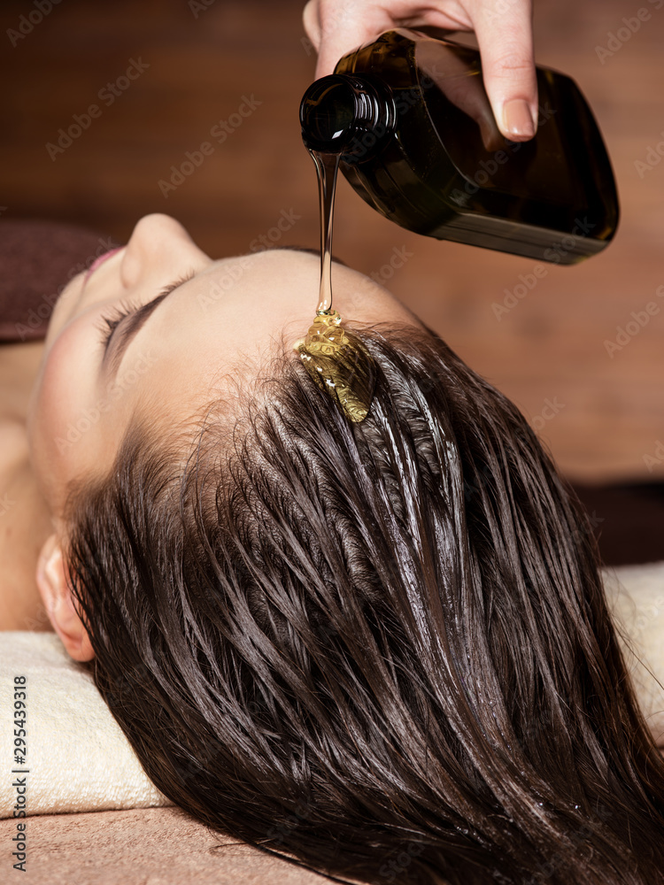 Cosmetologist pours balm for hair on head of  woman. Spa treatments. - obrazy, fototapety, plakaty 