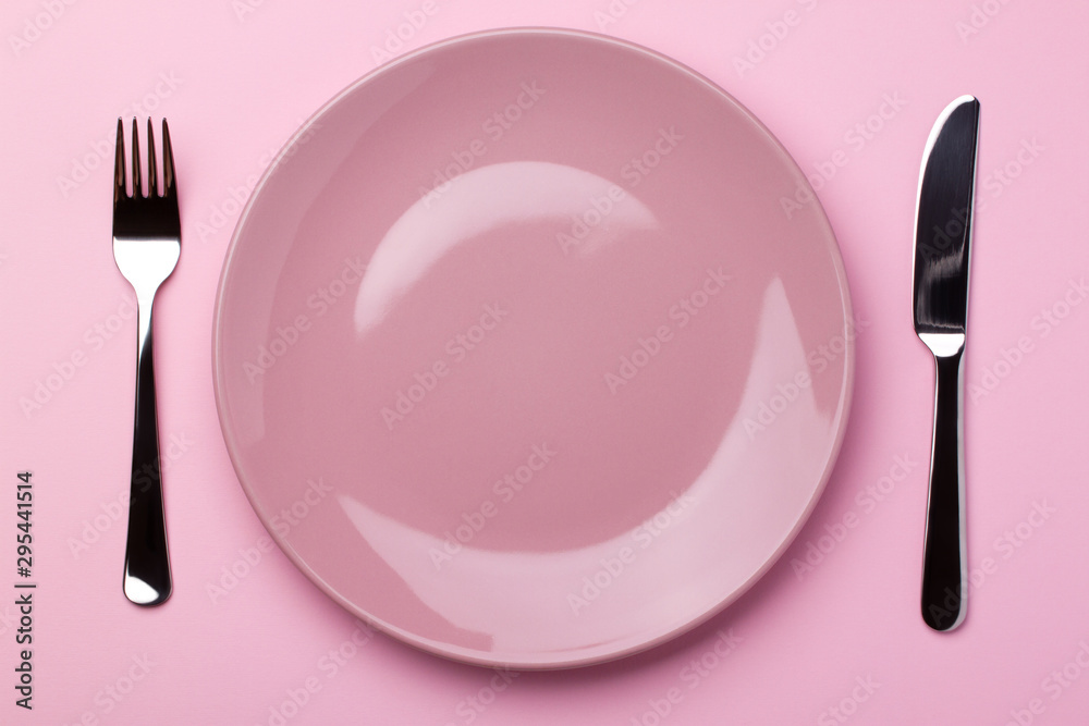 Pink glossy plate with metal cutlery - fork and knife around on a pink paper background. Pink glossy plate with metal cutlery - fork and knife around on a pink paper background.
