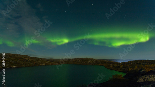 Northern lights, aurora in the sky above the hills and cliffs and reflected in the lake.
