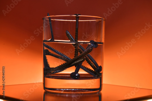 glass with screws on an orange background © константин константи