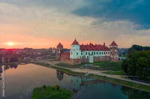 Mirsky Castle and its reflection in the lake in summer. Sunset in cloudy weather with rain clouds.