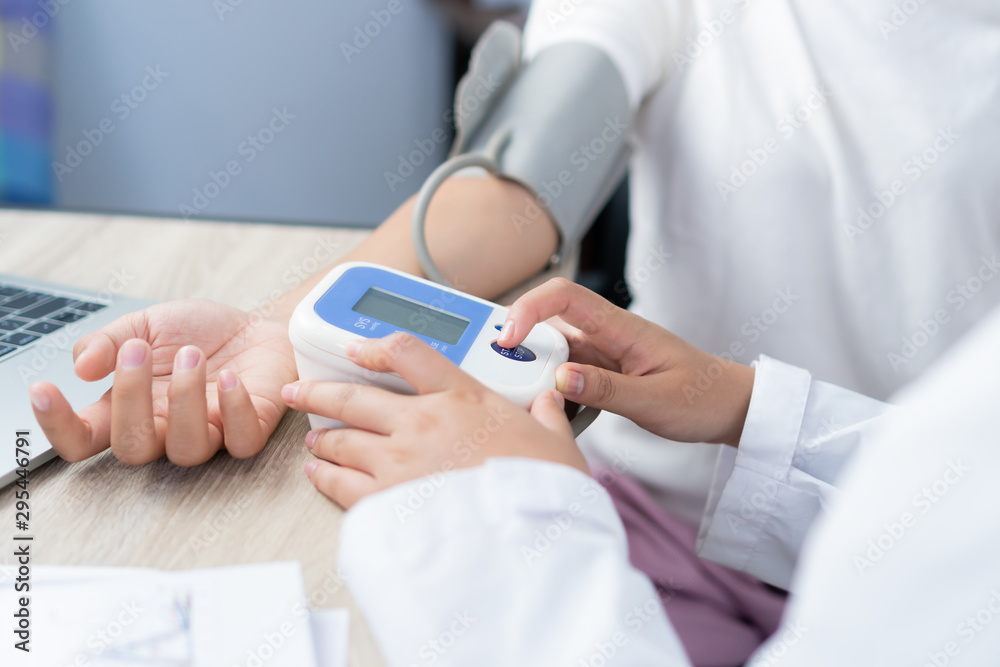 Healthcare in hospital and medicine concept : Doctor measuring blood pressure of young girl with pressure device monitor, in desk laptop computer consultation with gown stethoscope in clinic hospital Healthcare in hospital and medicine concept : Doctor measuring blood pressure of young girl with pressure device monitor, in desk laptop computer consultation with gown stethoscope in clinic hospital