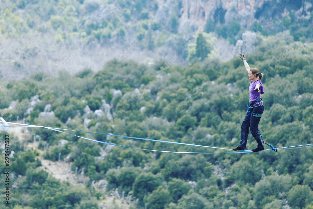 A woman is walking along a stretched sling. Highline in the mountains. Woman  catches balance. Performance of a tightrope walker in nature. Stock Photo