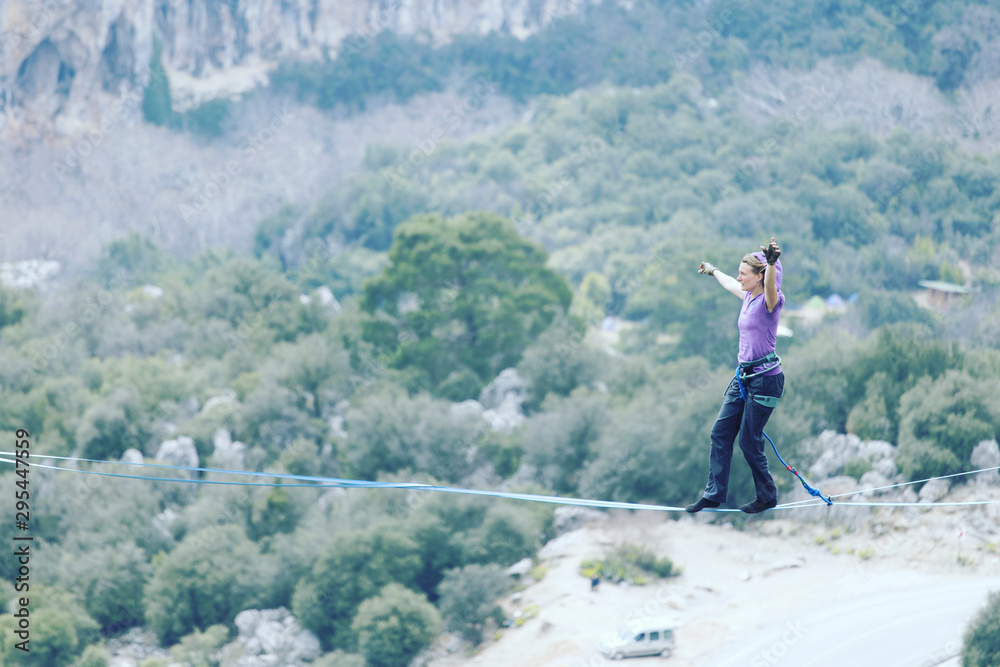 A woman is walking along a stretched sling. Highline in the mountains. Woman catches balance. Performance of a tightrope walker in nature.