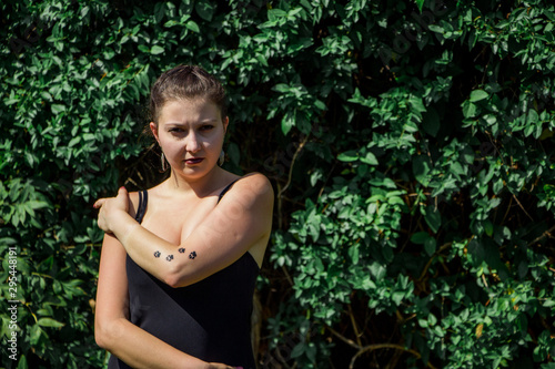 Young beautiful girl in black dress with tattoo on her hand in the park 