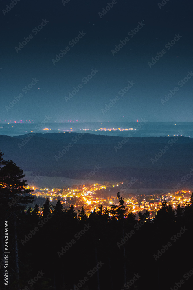 Glowing town in the mountains with the milky way galaxy and panorama mountain. view. Wurmberg, Braunlage Harz National Park, German Mountain
