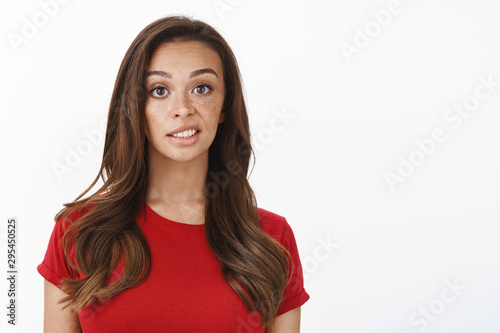 Skeptical displeased young picky feminine woman in red t-shirt, express disdain and scorn, look disappointed, slightly unsatisfied with result, standing white background reluctant