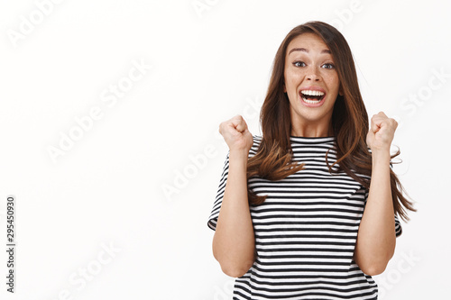 Ambitious lucky and hopeful cute girl winning lottery, jumping from happiness and joy, feeling relieved and upbeat, fist pump smiling camera and gazing astonished, triumphing white background