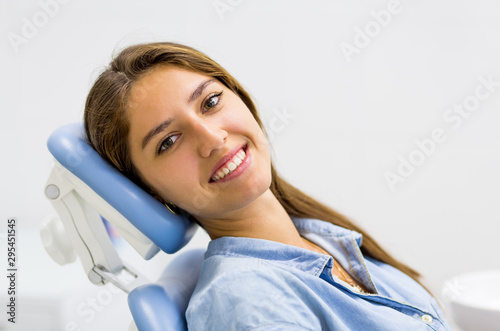 Young woman in blue jeans dress visiting the dentist and smiling sitting in dental chair.