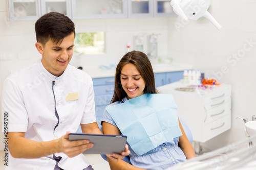 Male dentist in dental office talking with female patient and preparing for treatment. Filling in patient personal profile card.