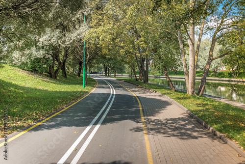 Bike path in the park with green trees. Beautiful summer landscape.