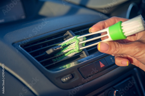 female hand with a brush for wiping dust on the dashboard of the car, a brush to remove dust in the vents from the air conditioner car © evgenii