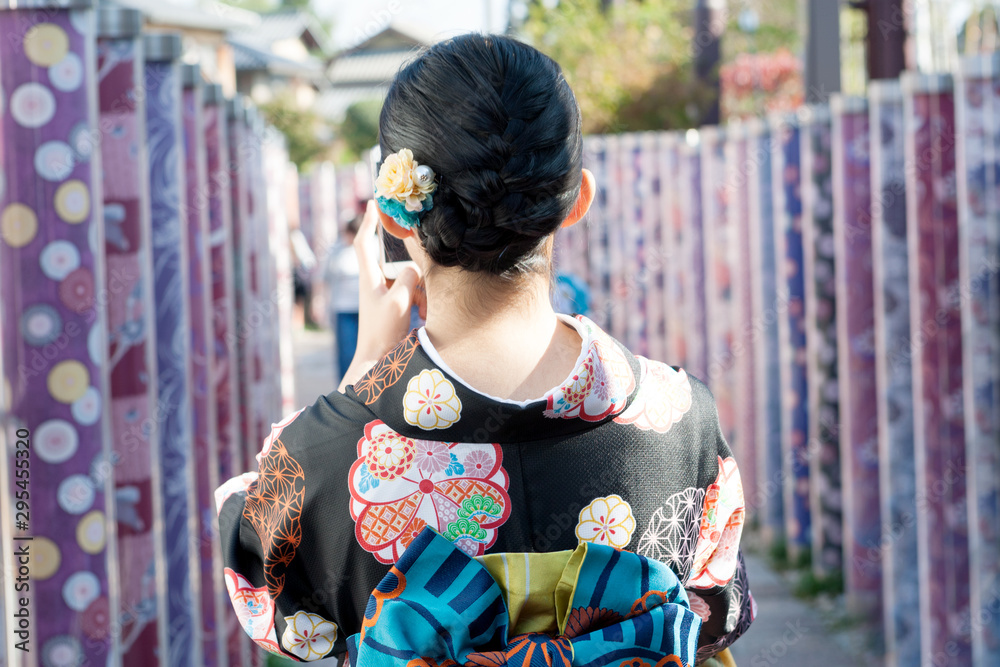 Back side of Japanese woman wearing kimono holding smartphone to  photograph that one has taken of oneself, typically one taken with a smartphone or webcam and uploaded to a social media website.