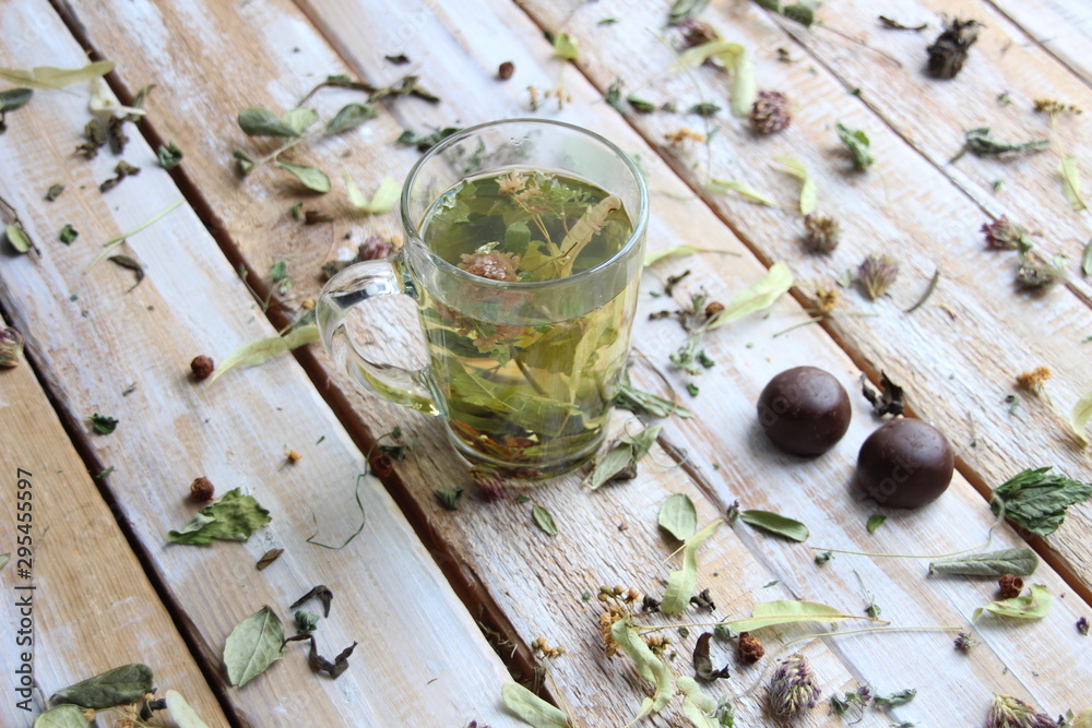 Glass with herbal tea on wooden background with dry herbs an chocolate sweets