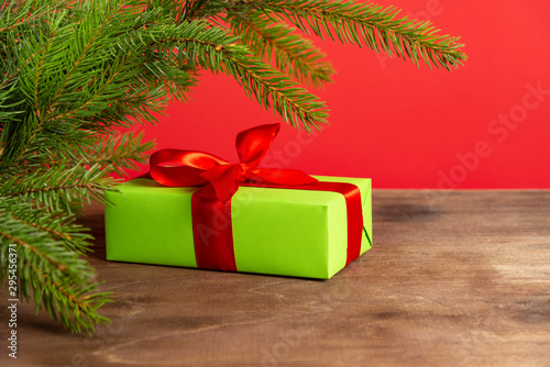 Christmas composition. Green gift box under the Christmas tree on a wooden table near a red background. a Christmas gift