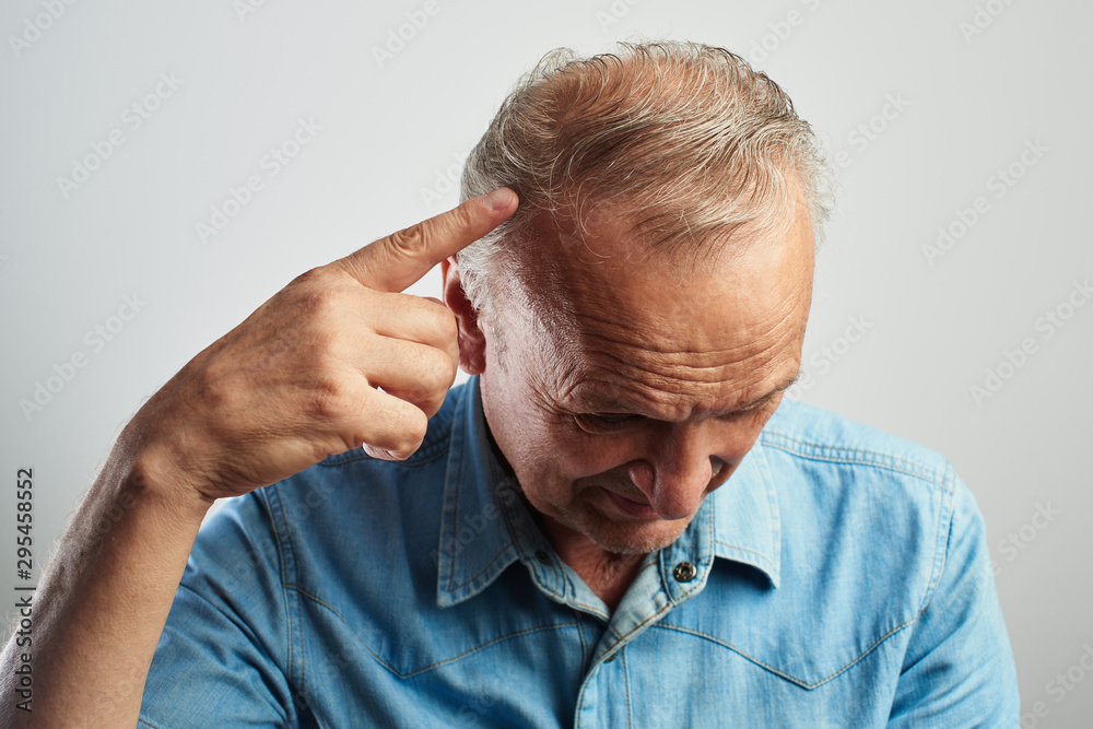 Fototapeta premium Pensioner points a finger at a gray-haired balding head isolated on a white background. The problem of hair loss, androgenic alopecia