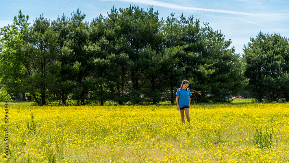 Teen girl standing in large field with yellow flowers and trees in the background Teen girl standing in large field with yellow flowers and trees in the background