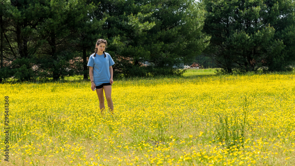 Teen girl standing in large field with yellow flowers and trees in the background