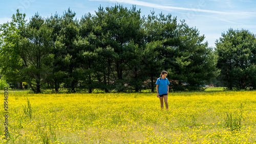 Teen girl standing in large field with yellow flowers and trees in the background