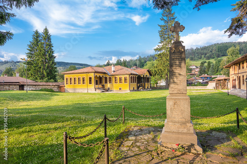 Monument with cross and characteristic yellow house on green lawn in koprivshtitsa photo