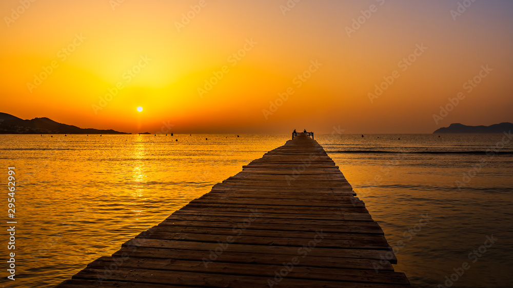 Solar disc in sunrise with silhouette of mountains and pier, panorama, Mallorca, Spain