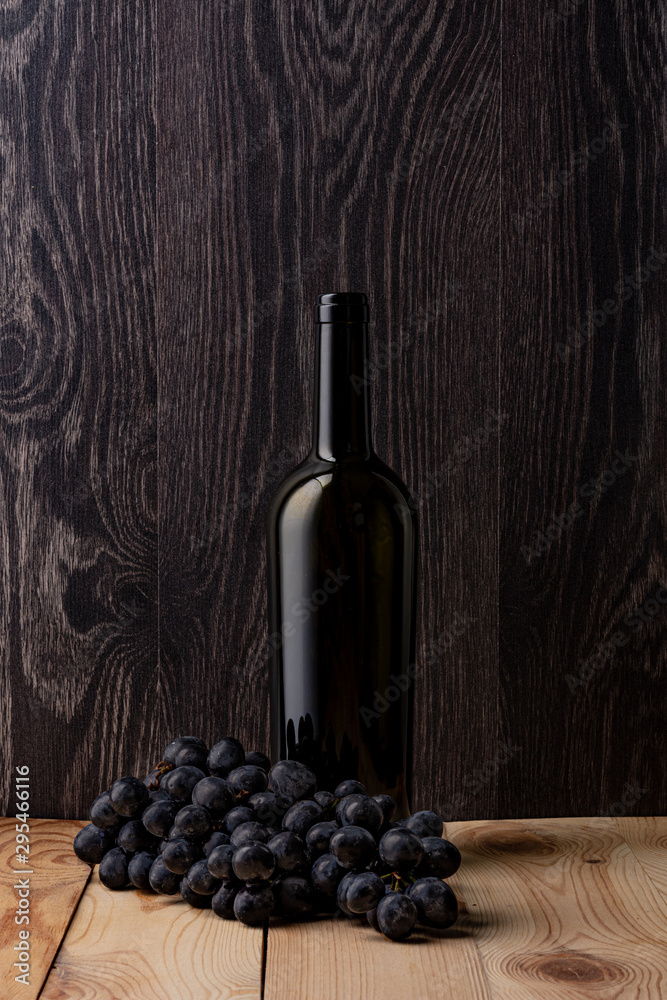 Wine bottle and a glass of wine. A bunch of ripe black grapes. Wooden background.