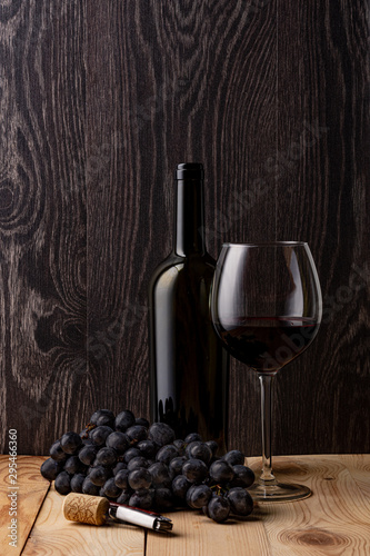 Wine bottle and a glass of wine. A bunch of ripe black grapes. Wooden background. Metal corkscrew. 