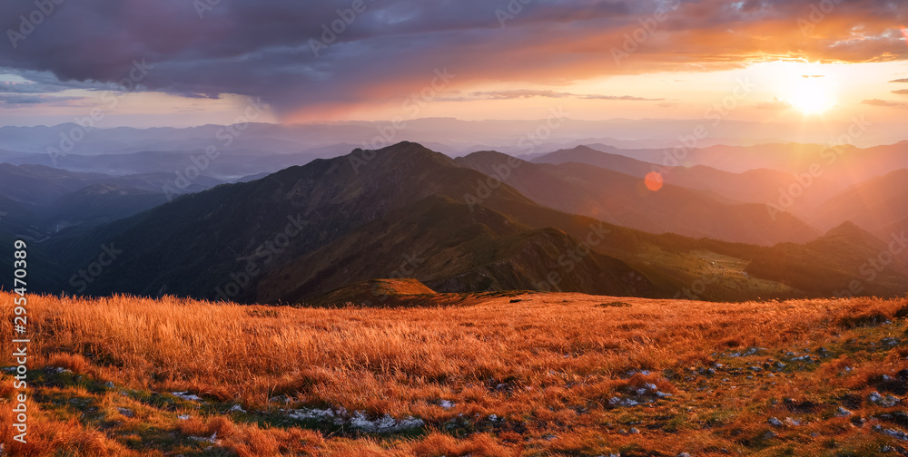 Autumn landscape. Amazing sunset enlightens surroundings. From the lawn in orange grass, a panoramic view of the high mountain, sky with clouds.
