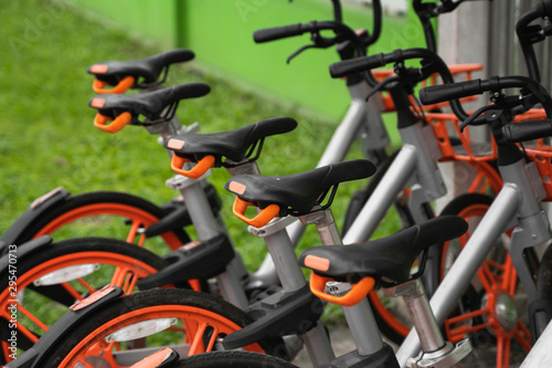 Street transportation orange hybrid rent bicycles with electronic form of payment for traveling around the city stand in row on rental network parking lot waiting for cyclists to make bike trip.