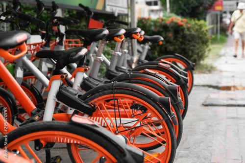Street transportation orange hybrid rent bicycles with electronic form of payment for traveling around the city stand in row on rental network parking lot waiting for cyclists to make bike trip.