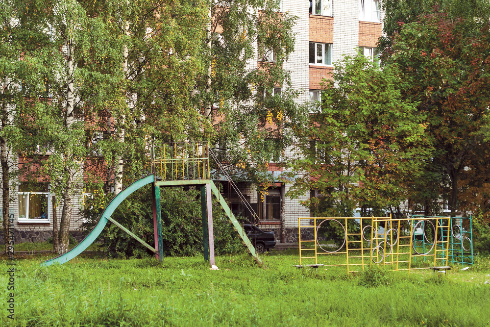 summer landscape with an old metal children’s slide in a poor Russian town summer landscape with an old metal children’s slide in a poor Russian town