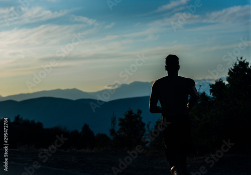 Fototapeta Naklejka Na Ścianę i Meble -  Full body portrait of a fit man running outdoors on a mountain road