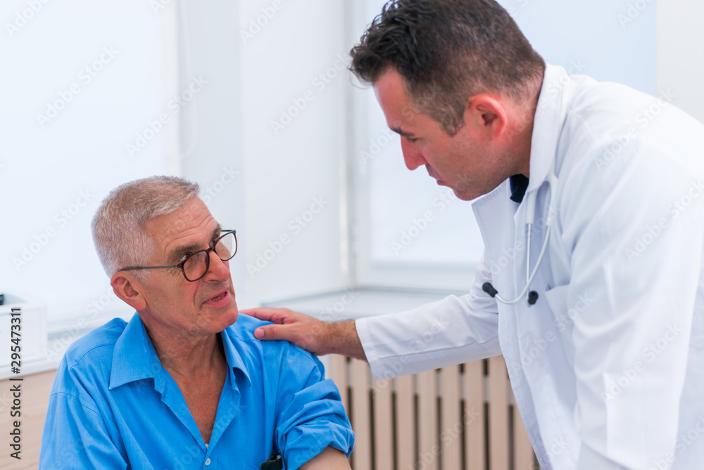 Middle aged caucasian doctor explains to his senior patient his blood pressure readings while standing next to him. Middle aged caucasian doctor explains to his senior patient his blood pressure readings while standing next to him.