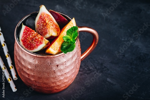 Fig moscow mule ice cold cocktail in copper cup with oranges and mint